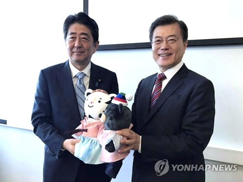 The file photo, taken Sept. 7, 2017, shows South Korean President Moon Jae-in (R) offering the mascots of the 2018 PyeongChang Winter Olympic Games to Japanese Prime Minister Shinzo Abe before the start of their bilateral summit on the sidelines of a regional economic forum in Vladivostok, Russia. (Yonhap)