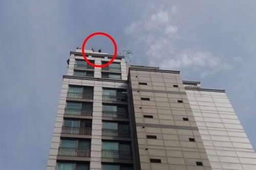 26일 서울 광진구 구의동의 한 20층짜리 주상복합단지 건물에서 중년 남성이 옥상에 올라가(빨간 원 안쪽 모습) 기물을 부수며 소동을 부리고 있다.[독자 제공=연합뉴스]