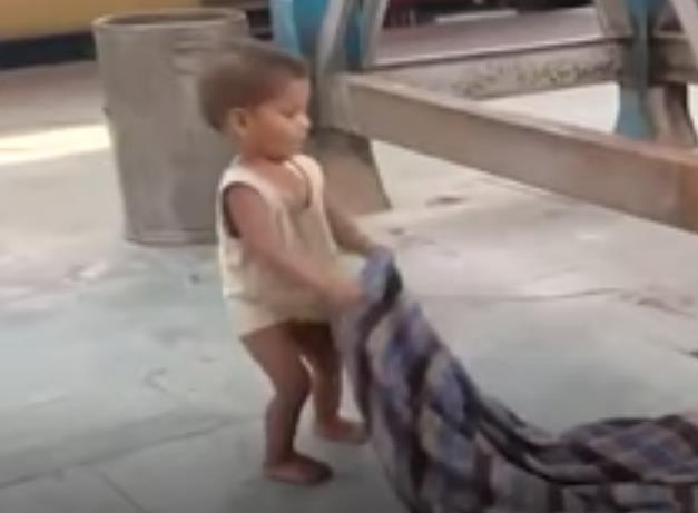 담요를 흔들어 엄마를 깨우려는 인도 기차역의 한 아기. [SNS 영상 캡처]