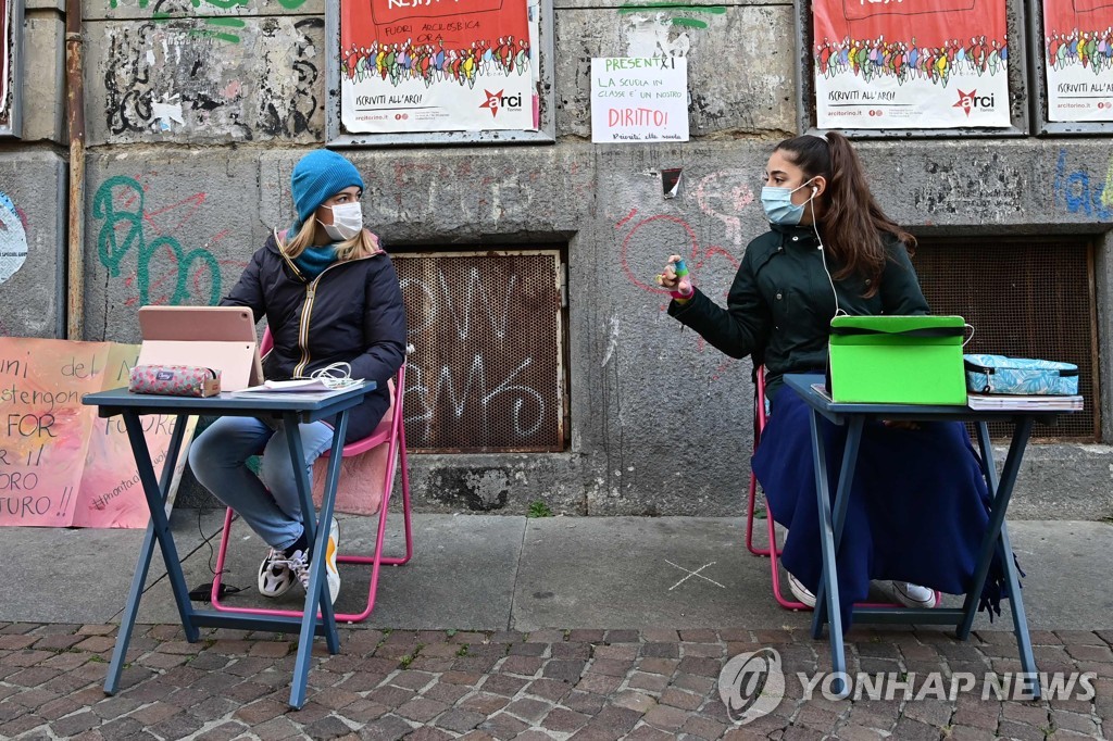 17일(현지시간) 이탈리아 토리노 시내에 있는 학교 밖 골목에 책상을 펴놓고 친구 리사 롤리아티(12)와 함께 원격 수업에 참여한 아니타 야코벨리(12). [AFP=연합뉴스]