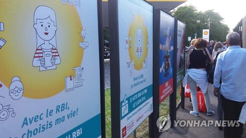 기본소득(Revenu de Base Inconditionne) 찬성 투표를 호소하는 포스터 앞을 지나 시내버스에 오르는 스위스 시민들.