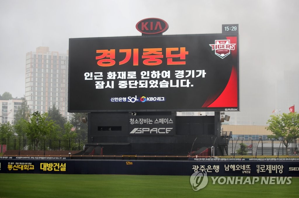 The scoreboard at Gwangju-Kia Champions Field in Gwangju, 330 kilometers south of Seoul, flashes a message on the suspension of the Korea Baseball Organization season opening game between the Kia Tigers and the Kiwoom Heroes, with black smoke from a fire near the stadium covering the field. (Yonhap)