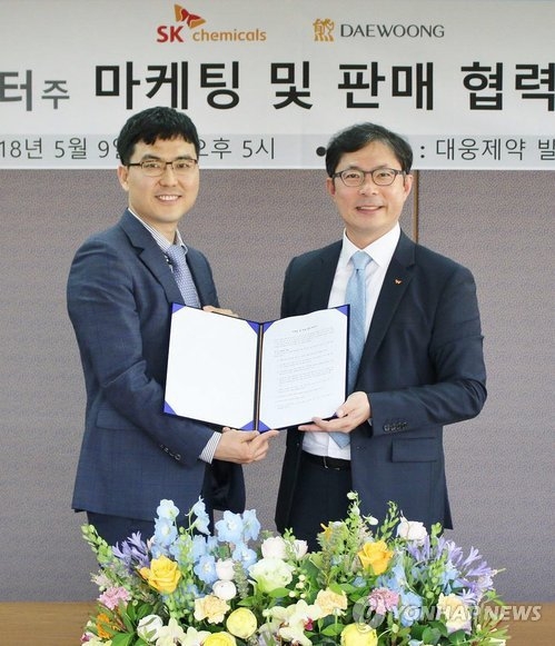 This photo provided by SK Chemicals Co. shows Ahn Jae-yong (R), an SK Chemicals official, holding the text of an agreement with Jeon Seung-ho, CEO of Daewoong Pharmaceutical Co. (Yonhap)
