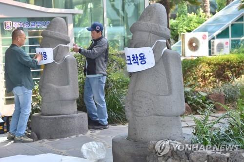 Officials in Jeju put masks on "dolhareubang" statues, a basalt totem statue that is a symbol of the tourist island, on April 28, 2020. (Yonhap)