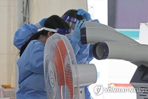 Medical workers stand in front of an evaporative air cooler at a COVID-19 test center in southern Seoul on May 19, 2021, amid early summer temperatures across the nation. (Yonhap)
