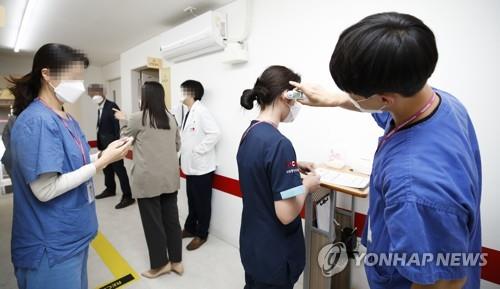 A medical worker (R) checks the body temperature of people who are set to receive additional vaccine jabs at a vaccination center in Seoul on Oct. 12, 2021. Health authorities started giving additional COVID-19 shots to people who were fully vaccinated six months ago the same day. (Pool photo) (Yonhap)
