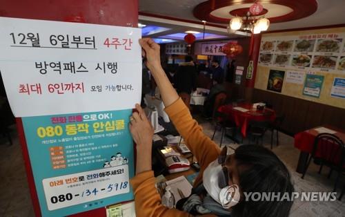 An employee attaches a notice to the entrance of a Chinese restaurant in Seoul on Dec. 3, 2021, that says a customer is required to show proof of vaccination or a negative test for entry and that gatherings are limited to six people starting Dec. 6. South Korea said it will limit private gatherings to six people in the capital area and eight in other regions for four weeks, reversing an easing of distancing rules adopted under the "living with COVID-19" scheme last month. (Yonhap)
