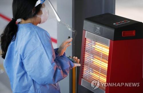 A medical worker warms her hands at a makeshift COVID-19 testing station the southwestern city of Gwangju on Feb. 22, 2022, in this photo provided by a local government. (PHOTO NOT FOR SALE) (Yonhap)