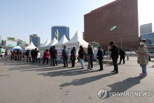 People stand in line to take coronavirus tests at a makeshift testing site in front of Seoul Station on March 27, 2022. South Korea reported 318,130 new virus cases on the day. (Yonhap)