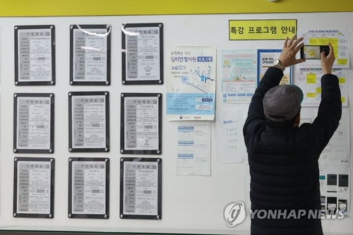 Un homme âgé prend une photo d'informations sur un tableau d'affichage d'un centre d'emploi à Mapo, à l'ouest de Séoul, le 15 mars 2023.