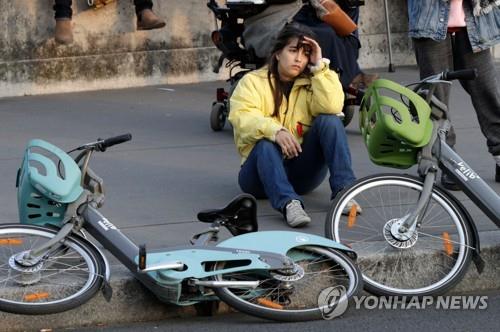 15일(현지시간) 파리 노트르담 대성당에서 큰불이 나자 지나가던 여성이 자전거를 놓고 현장을 바라보고 있다. [AFP=연합뉴스]