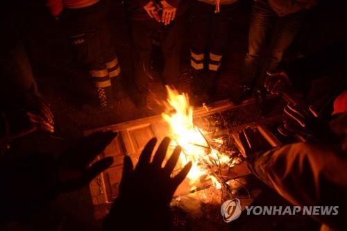 24일 강력한 지진이 발생한 터키 동부 엘라지에서 구조대원들이 불을 쬐며 몸을 녹이고 있다. [AFP=연합뉴스] 