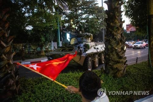 양곤 시내를 이동하는 장갑차 옆으로 한 시민이 깃발을 흔들고 있다. 2021.2.14