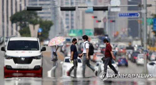Los peatones cruzan una calle en Yeouido, en el oeste de Seúl, el 22 de junio de 2020, mientras que se puede ver un espejismo de calor debido a las altas temperaturas en la capital surcoreana, que se situaron por encima de los 35 grados centígrados.