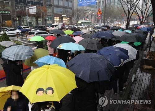 Los ciudadanos esperan en fila bajo la lluvia para ser examinados del coronavirus, el 30 de noviembre de 2021, en una clínica provisional en el distrito de Songpa, en Seúl.