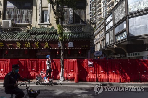(AP=연합뉴스) 지난 9일 중국 광둥성 광저우에서 한 주민이 코로나19로 봉쇄된 지역 앞에 처진 바리케이드 너머로 물건을 넘겨주는 모습. 2022.11.15.
