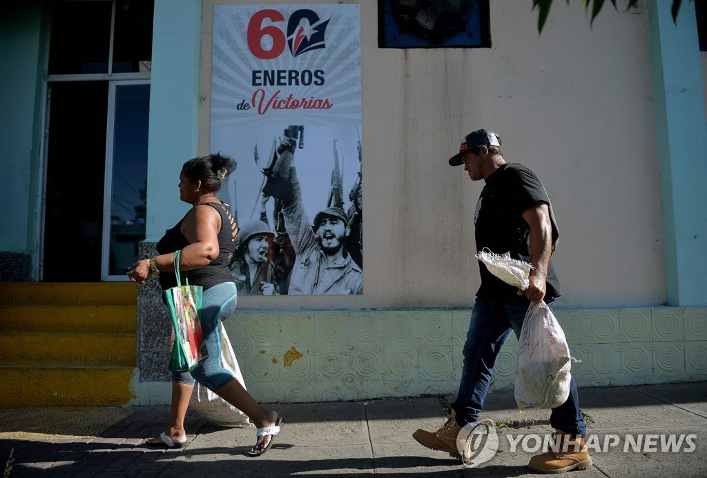 쿠바 혁명 60주년을 기념하는 포스터 옆을 지나가는 산티아고 데 쿠바 시민들 [AFP=연합뉴스] 