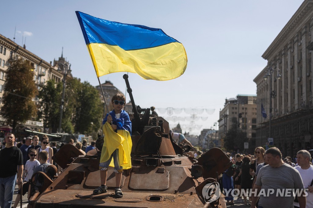 21일(현지시간) 한 소년이 키이우 거리에 전시된 러시아군 군용 차량 위에서 우크라이나 국기를 흔들고 있다.