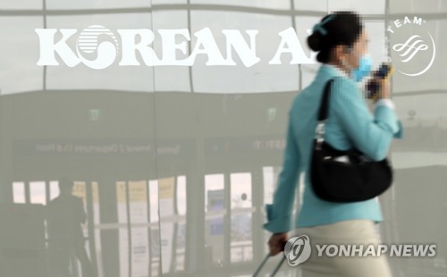 This photo taken on Feb. 25, 2020 shows a flight attendant passing by Korean Air's company logo at the No. 2 terminal of the Incheon International Airport in Incheon, just west of Seoul. (Yonhap)