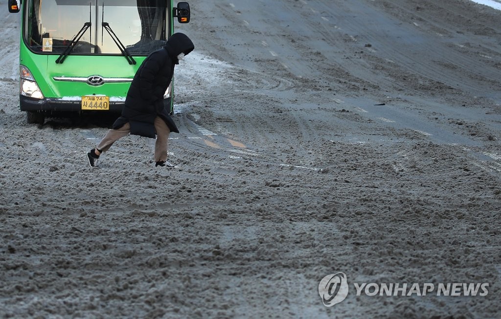 A person walks across a slushy road in southern Seoul on Jan. 7, 2021. (Yonhap)