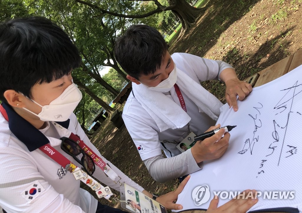 South Korean archer Kim Je-deok (R) signs his uniform at Yumenoshima Park Archery Field in Tokyo on July 31, 2021, before donating it to the International Olympic Committee's Olympic Museum in Switzerland, in the photo provided by the Korea Archery Association on Aug. 1. (PHOTO NOT FOR SALE) (Yonhap)