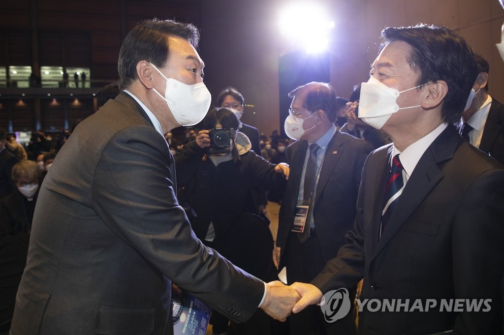 This pool photo taken on Dec. 10, 2021, shows the People Power Party's presidential candidate Yoon Seok-yeol (L) shaking hands with People's Party nominee Ahn Cheol-soo at an event at COEX in Seoul. (Yonhap)