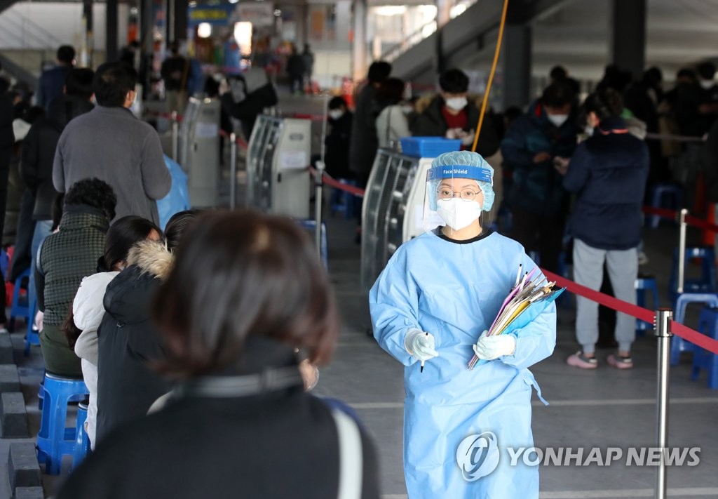 La foto, tomada el 3 de enero de 2022, muestra a una trabajadora médica guiando a las personas que esperan para someterse a las pruebas del nuevo coronavirus, en una clínica provisional, en la ciudad sudoriental de Gwangju.