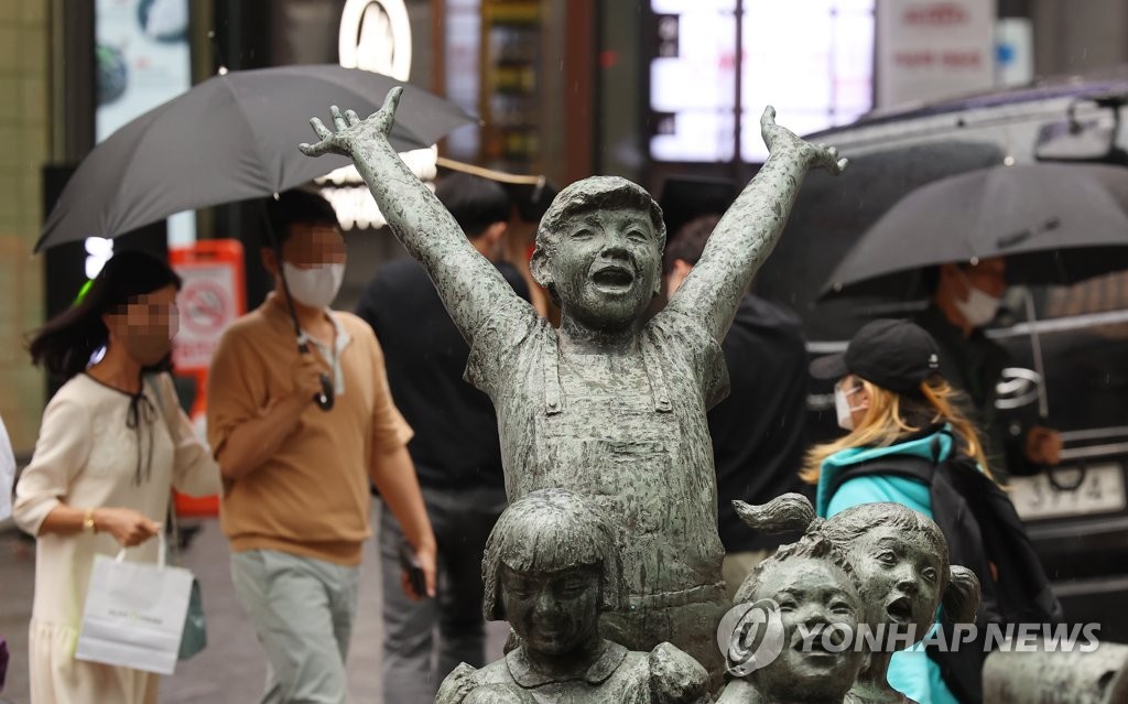 지난 10일 오후 서울 명동 거리에서 우산을 쓴 시민이 환하게 웃고 있는 어린이 동상 뒤를 지나고 있다. [연합뉴스 자료사진]