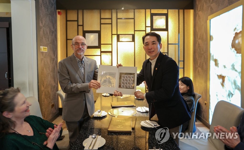 This photo, provided by the veterans ministry on Feb. 6, 2023, shows Veterans Minister Park Min-shik (R) handing postal stamps commemorating Ernest Bethell, who reported on Imperial Japan's misdeeds against Korea, to his grandson as they meet at a restaurant in London on Feb. 4, 2023. (PHOTO NOT FOR SALE) (Yonhap)