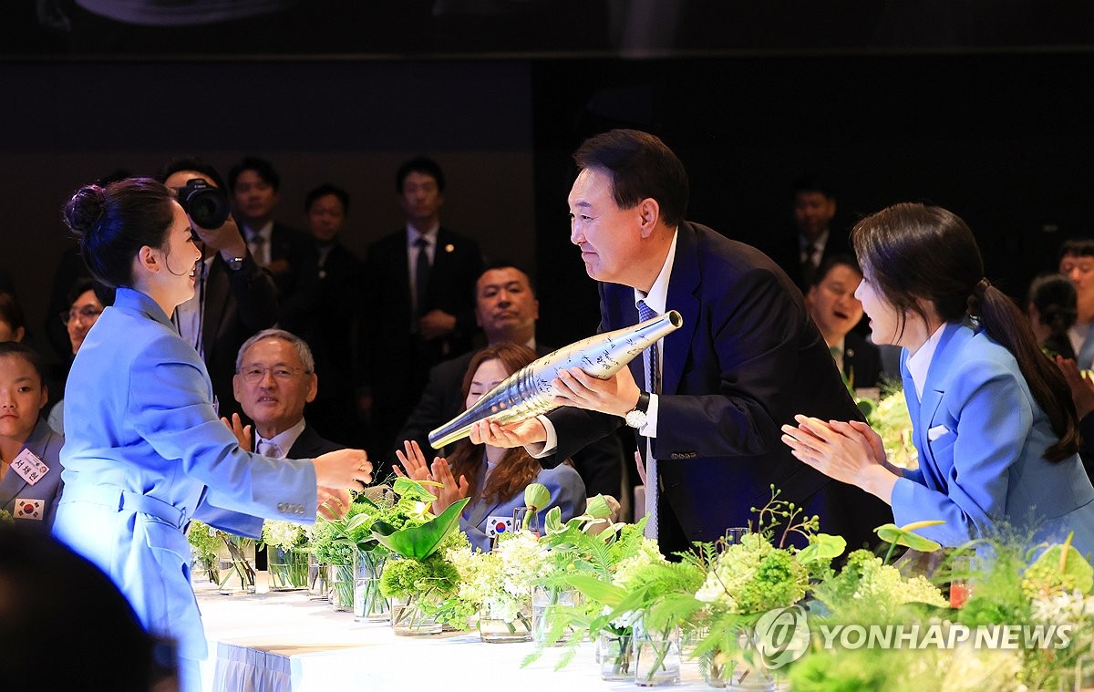 La medallista olímpica de tenis de mesa de Corea del Sur, Jeon Ji-hee (izq.), entrega al presidente Yoon Suk Yeol (centro) la antorcha olímpica de París firmada por atletas surcoreanos durante una cena organizada por la oficina presidencial en un hotel de Seúl el 22 de agosto de 2024, en esta foto proporcionada por la oficina. (FOTO NO A LA VENTA) (Yonhap)